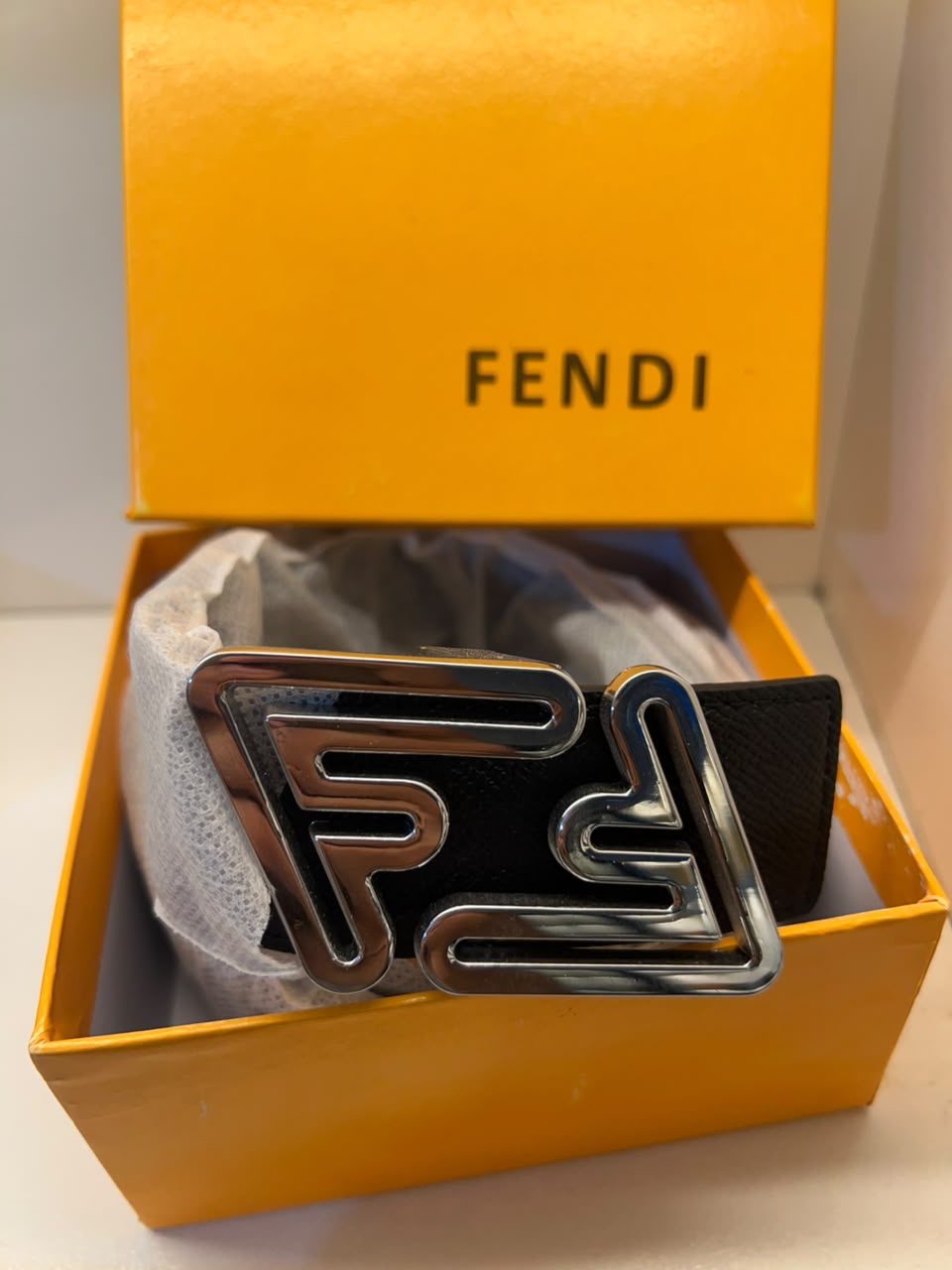 A Fendi belt with a large, polished silver-tone double-F logo buckle, presented inside its signature orange Fendi gift box.